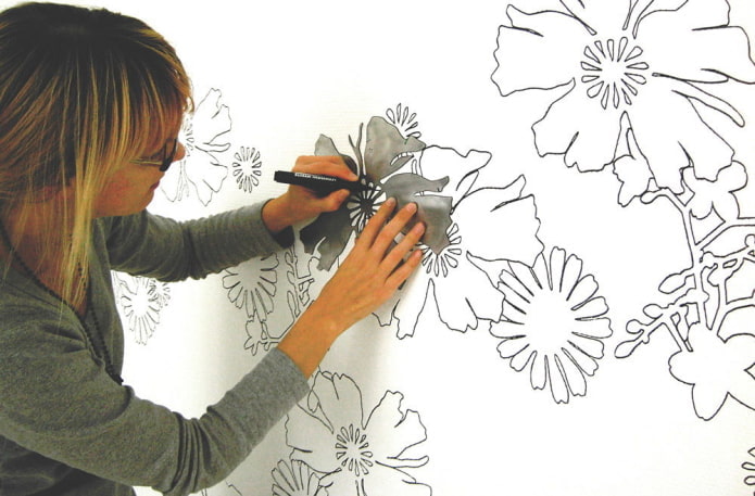 donna che dipinge fiori sul muro usando uno stencil